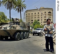 Australian troops aboard an armoured personnel vehicle pass by a checkpoint guarded by an Iraqi policeman at a a href=