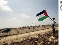 Palestinian boy holds a flag in West Bank village of Bilin as an Israeli army vehicle passes by a section of separation barrier during celebrations of Israeli a href=